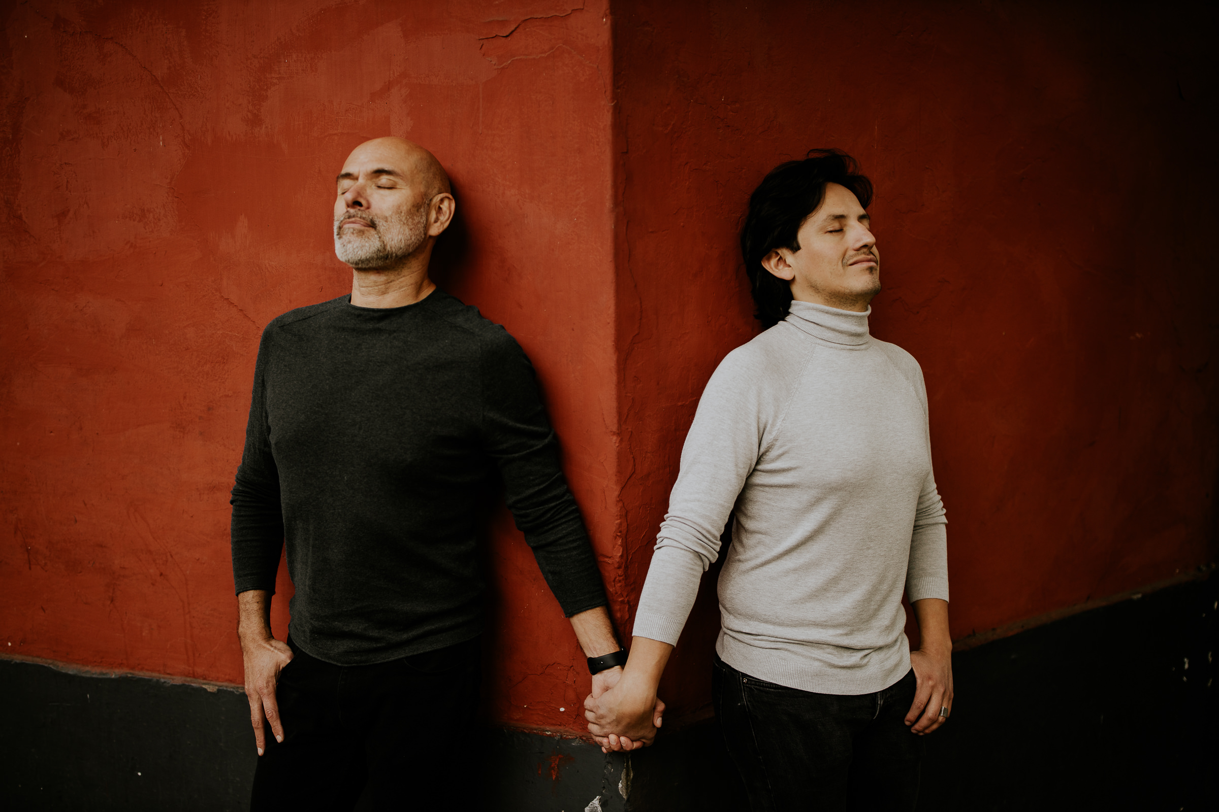 two men holding hands in front of a red wall